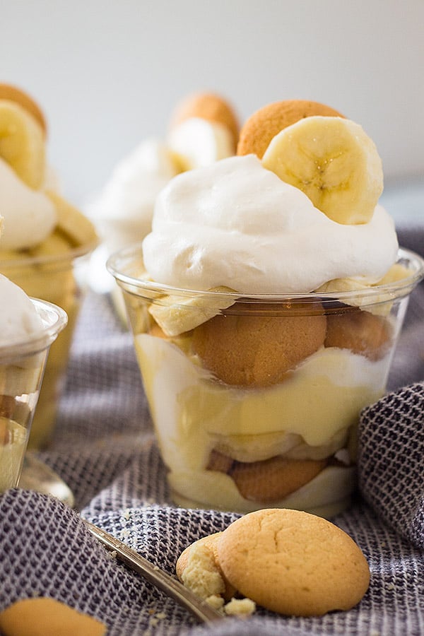 Plastic cups with banana pudding layers sitting on white and blue towel. 