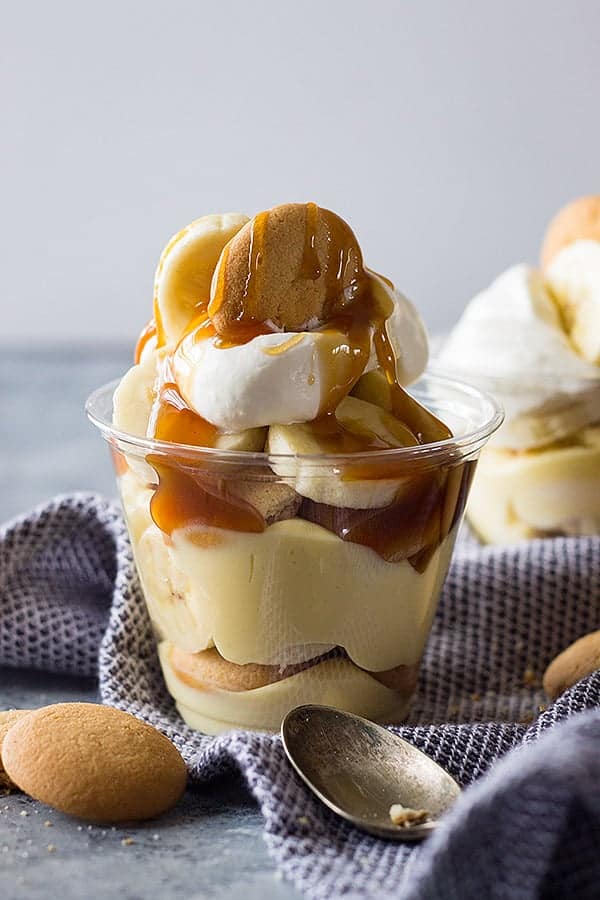 Homemade banana pudding cup drizzle with caramel and sitting on blue kitchen towel. 