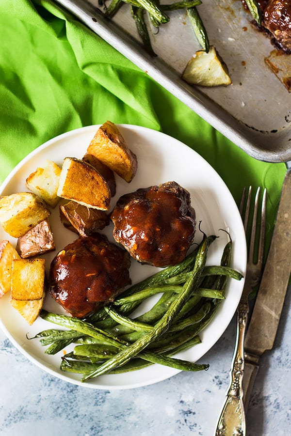 sheet pan bbq meatballs and vegetables on a white plate with cutlery beside it