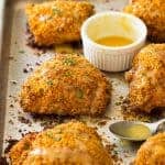 Crispy baked chicken thighs on a sheet pan with a honey mustard sauce beside.