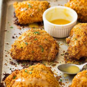 Crispy baked chicken thighs on a sheet pan with a honey mustard sauce beside.