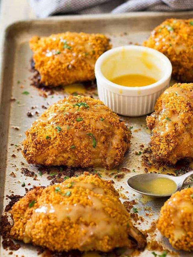 Crispy baked chicken thighs on a sheet pan with a honey mustard sauce beside.