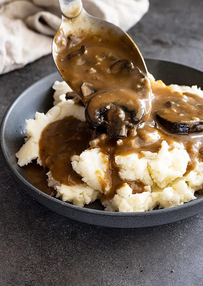 Gravy being spooned over mashed potatoes.