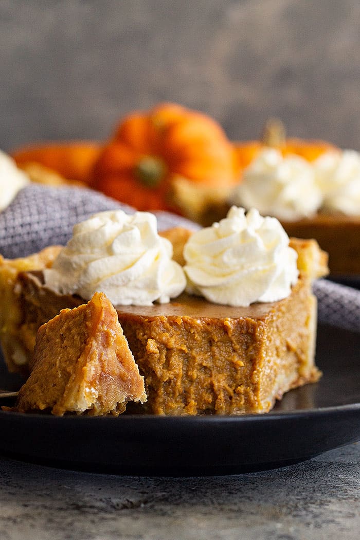 Close up of a slice of traditional pumpkin pie with a bite taken out to show how smooth and creamy it is.