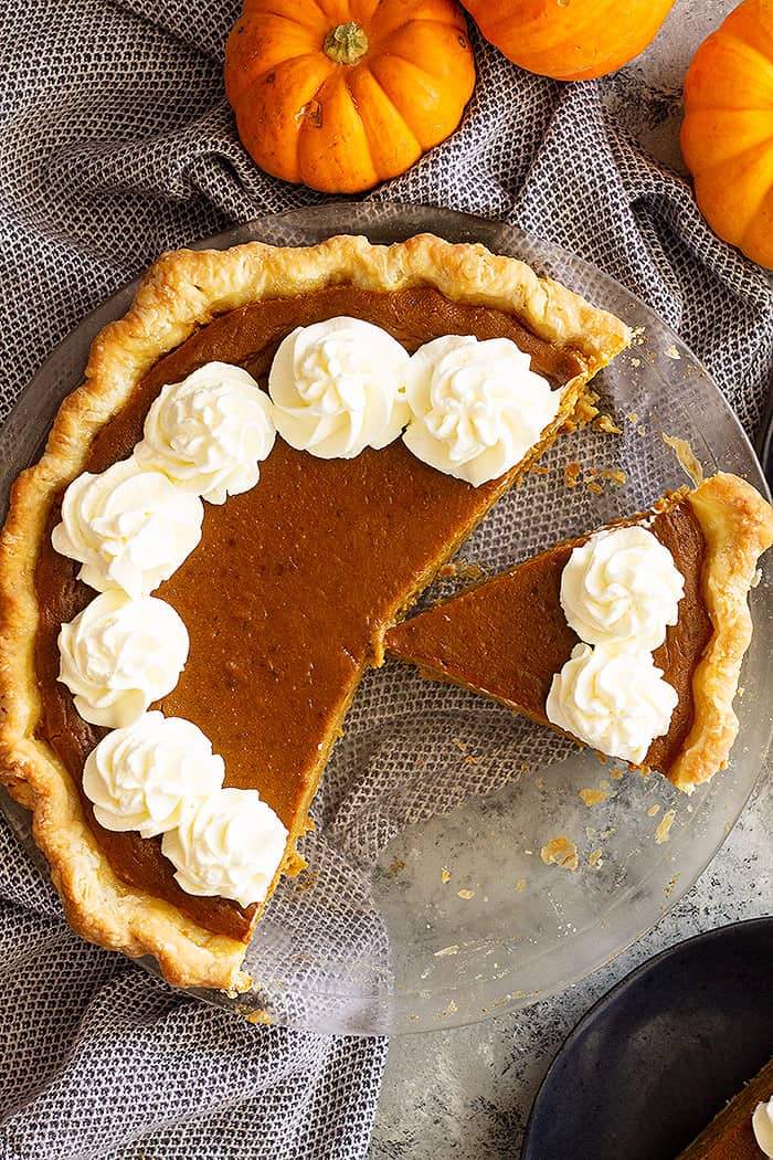 Top down view of a traditional pumpkin pie with slices taken out. Garnished with whipped cream around the edge of the pie. 