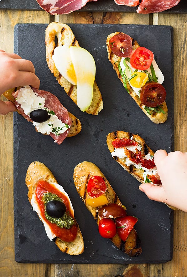 Hands picking up slices of bruschetta off of a black slate board. 