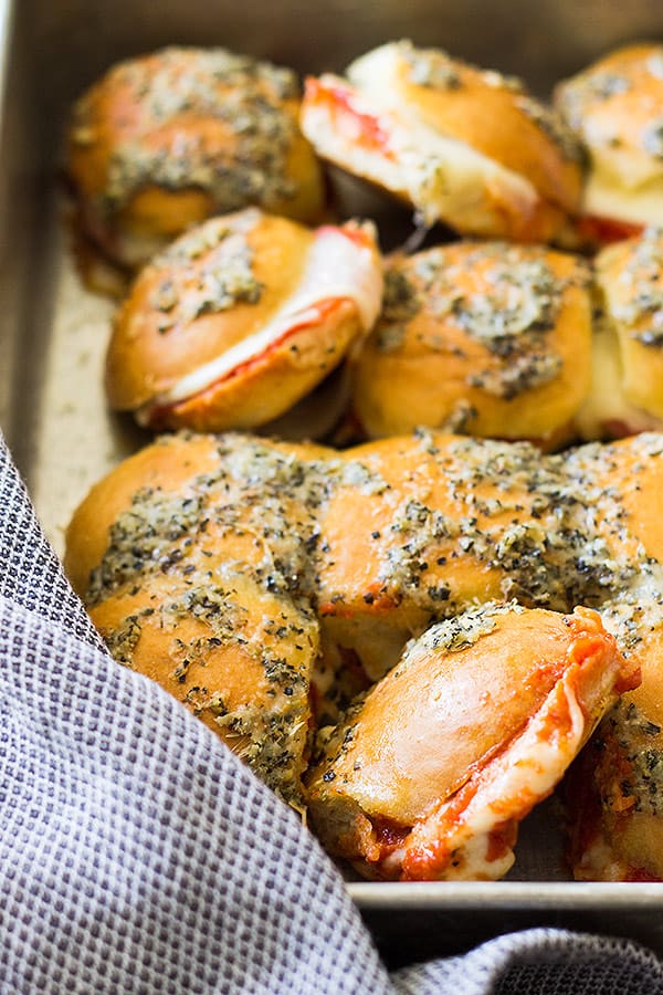 A large pan of pepperoni pizza sliders topped with cheese and herbs. 