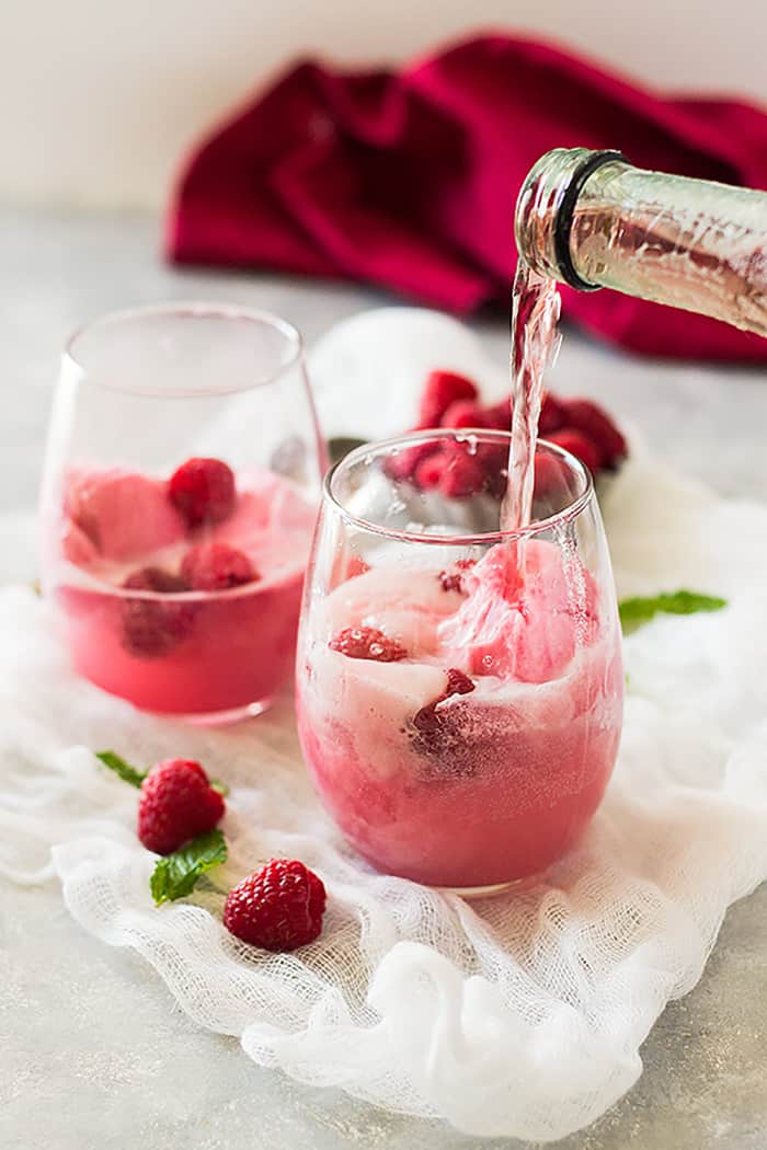 Two glasses with raspberry sherbet and fresh raspberries and pink champagne being poured into each. 