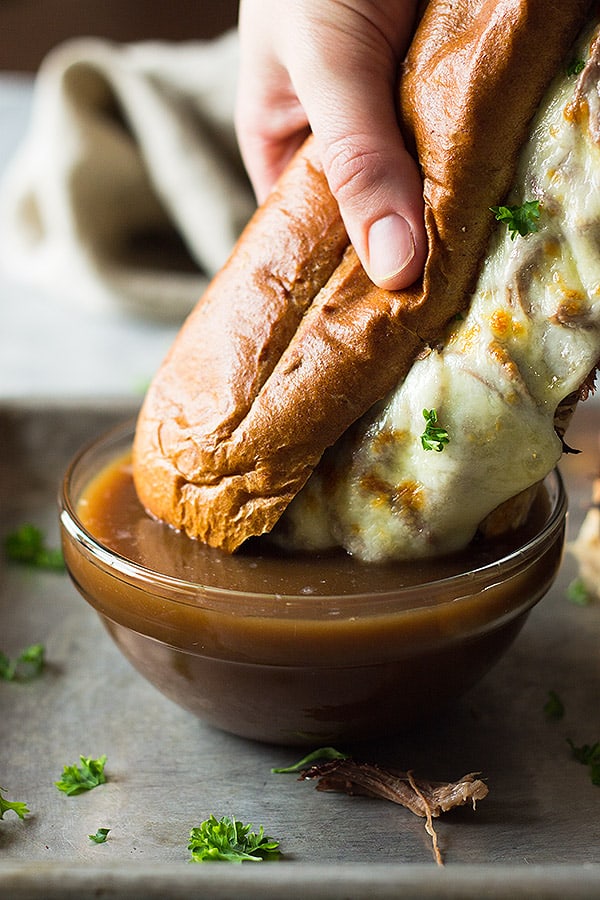 A french dip sandwich dipping into a bowl of au jus. 