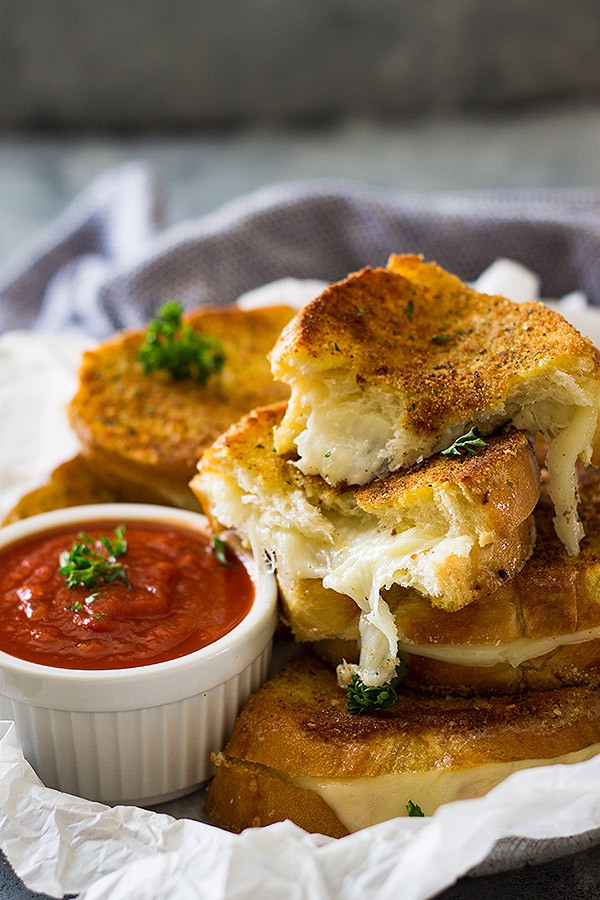 Sliced grilled cheese sandwiches next to small while bowl of pizza sauce.