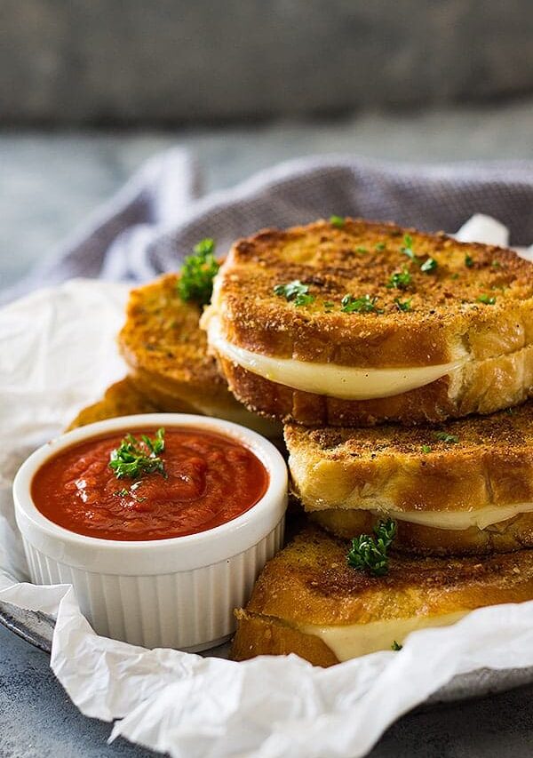 Grilled cheese sandwiches next to small while bowl of pizza sauce.
