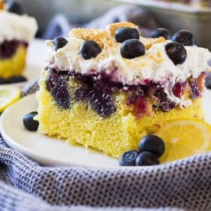 One piece of lemon blueberry poke cake on white plate with blueberries