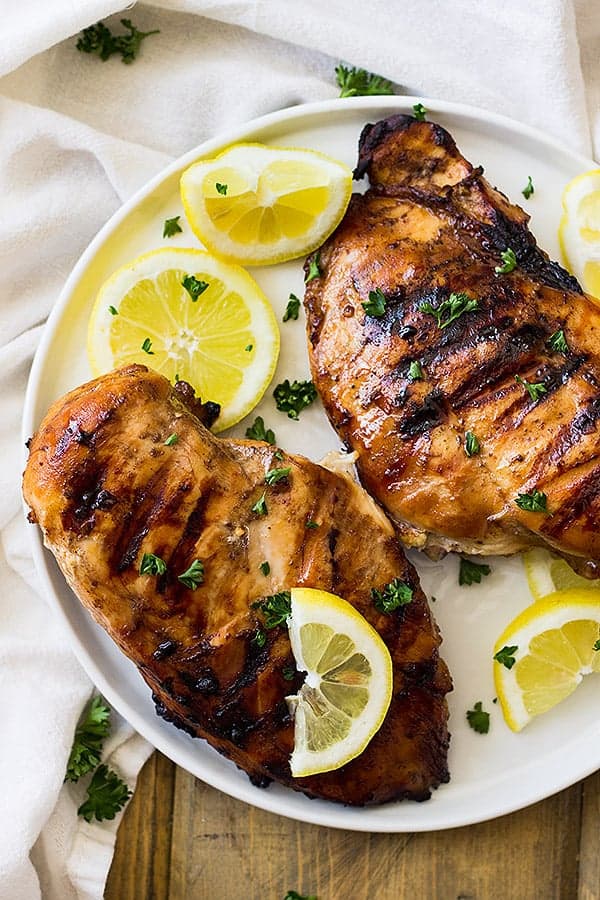 Two chicken breasts on white plate with lemon wedges after marinating in simple marinade for chicken