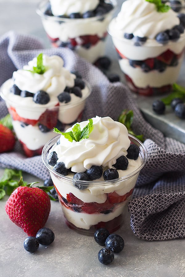 Berry Cheesecake Cups sitting on blue kitchen towel with berries on counter.