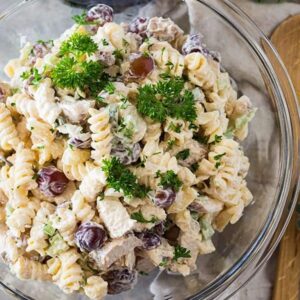 top shot of pasta salad with red grapes in clear glass mixing bowl
