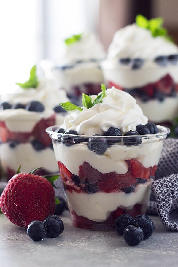 Eye level view of berry cheesecake cups with blue towel and more cups behind it.
