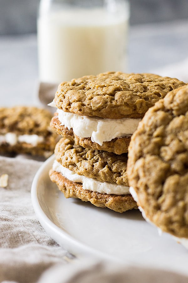 Oatmeal cream pies stacked on plate with glass of milk in background. 