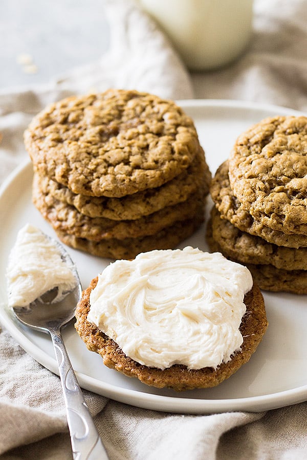 Vanilla frosting spread on oatmeal cookie with more cookies stacked behind it. 