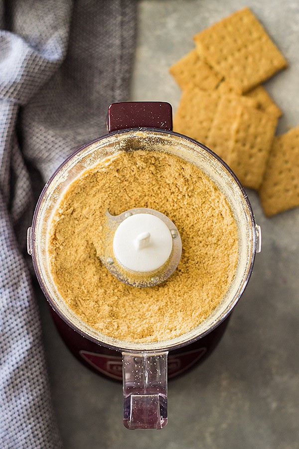 Food processor with ground graham cracker crumbs and full crackers in background. 