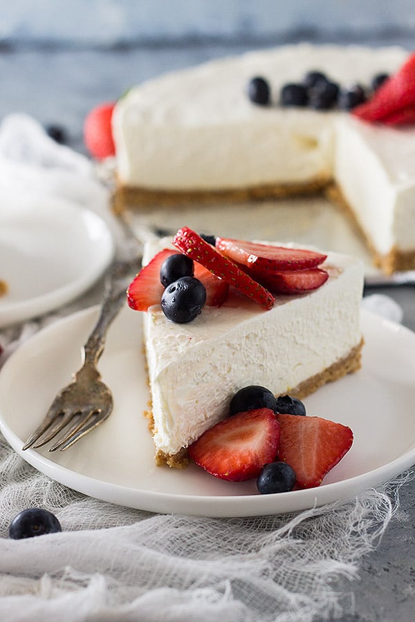 Slice of no bake cheesecake on white plate with fresh berries. 