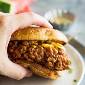 hand holding slow cooker beef and bean sloppy joes above white plate