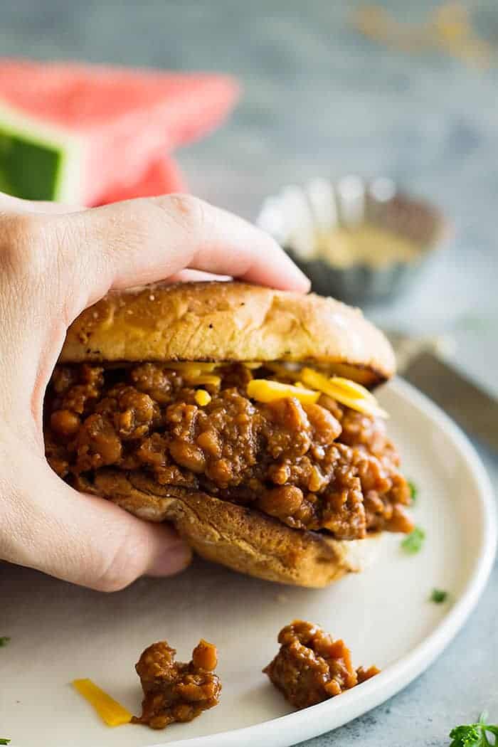 hand holding slow cooker beef and bean sloppy joes above white plate