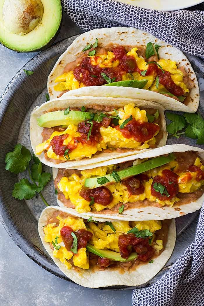 Top down view of Bean and Cheese breakfast tacos topped with salsa and avocado slices. 