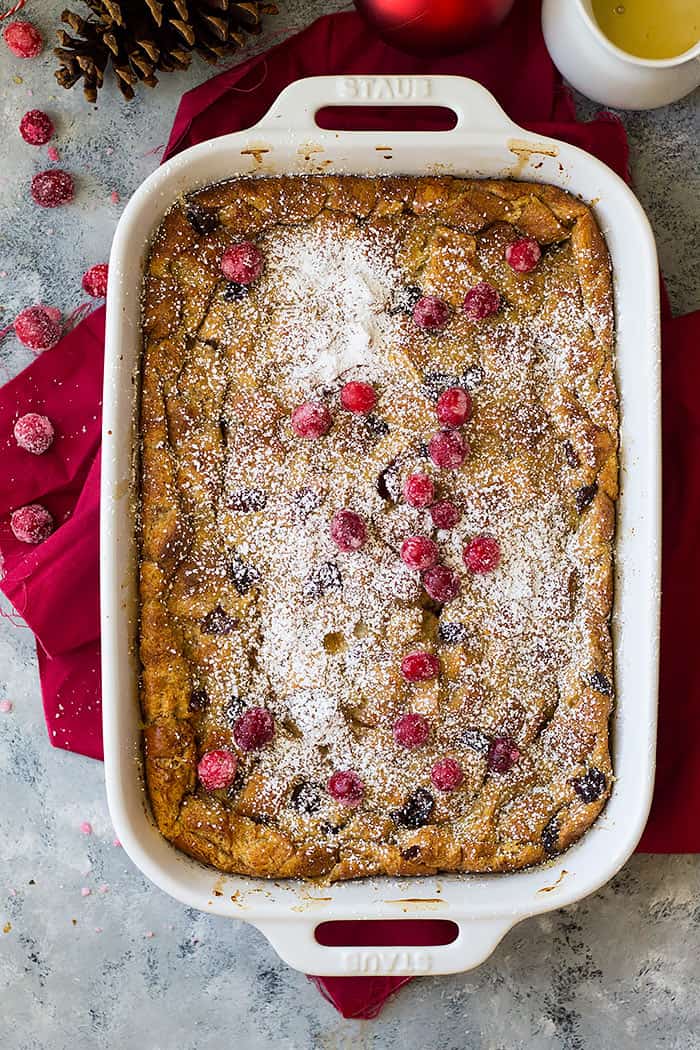 Top down view of cranberry bread pudding in a casserole dish topped with powdered sugar and sugared cranberries. 