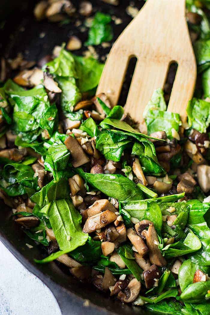 Chopped mushrooms and spinach in a skillet cooking.