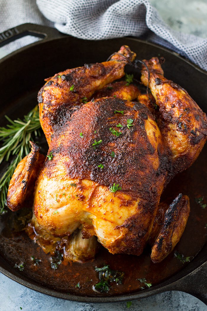 Whole oven roasted chicken in cast iron skillet with fresh herbs on top. 