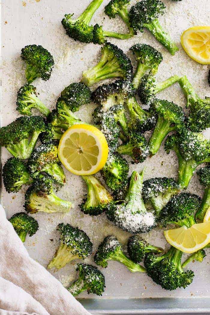 Top down view of lemon parmesan roasted broccoli on a sheet pan with lemon slices.