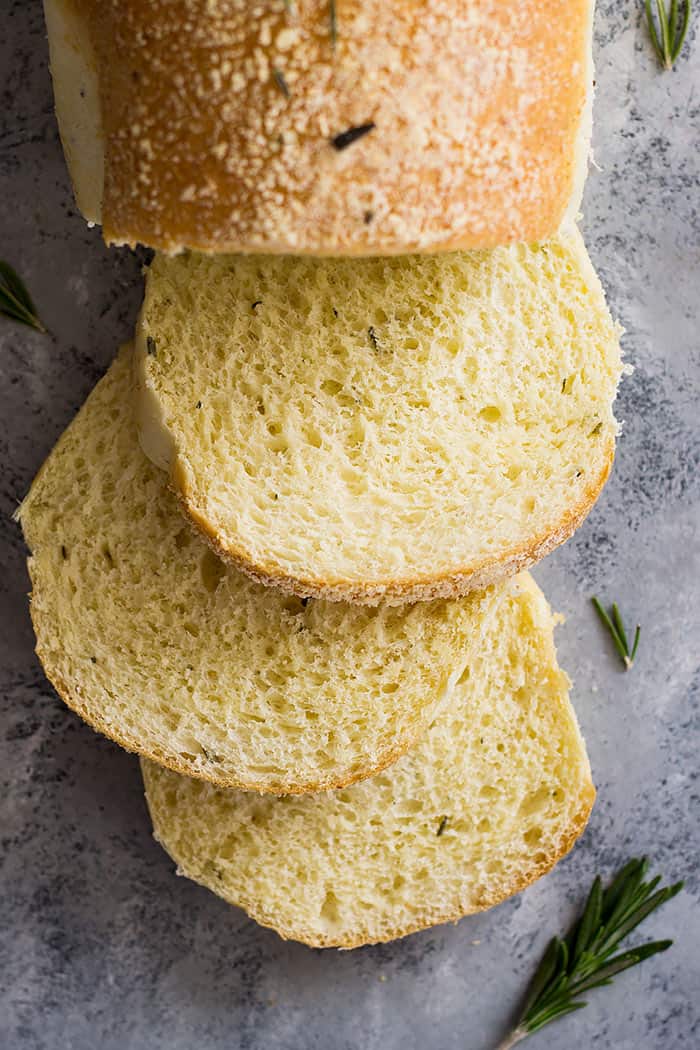 Slices of rosemary parmesan bread beside a loaf of bread.
