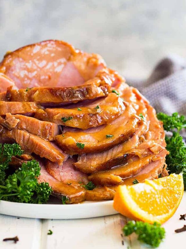 Slow cooker honey mustard glazed ham sliced and stacked tall on a plate. Garnished with chopped parsley.