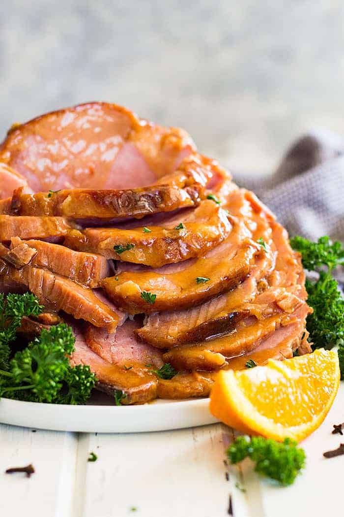 Slow cooker honey mustard glazed ham sliced and stacked tall on a plate. Garnished with chopped parsley.