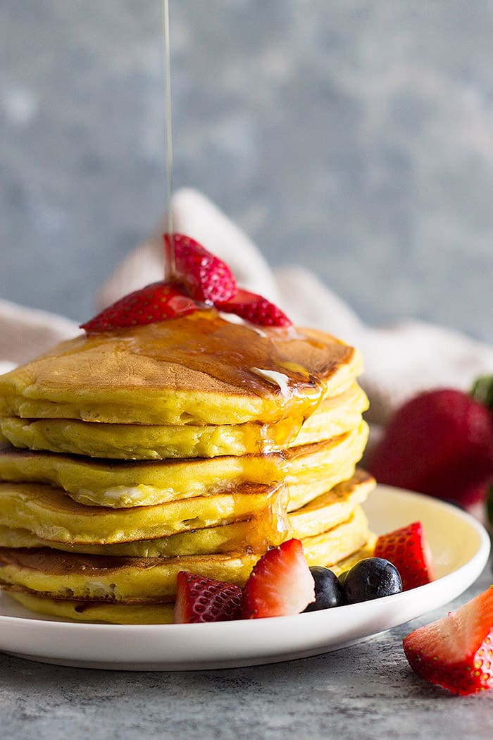Stack of high protein cottage cheese pancakes drizzled with syrup and fruit. 