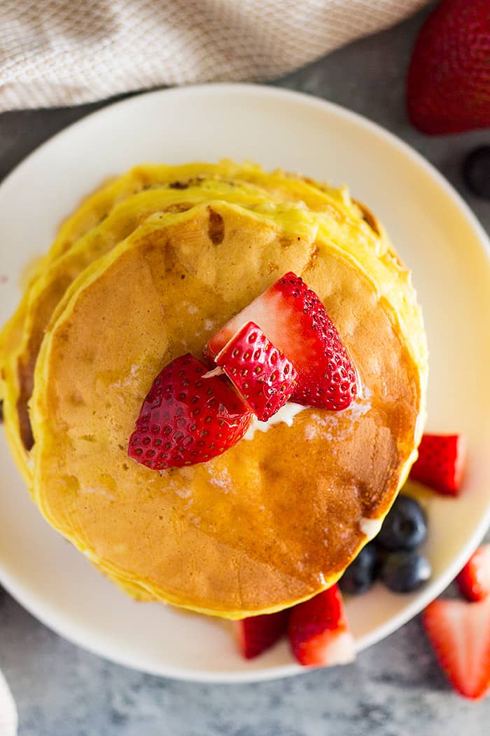 A top down view of a stack of high protein cottage cheese pancakes with fruit on top.