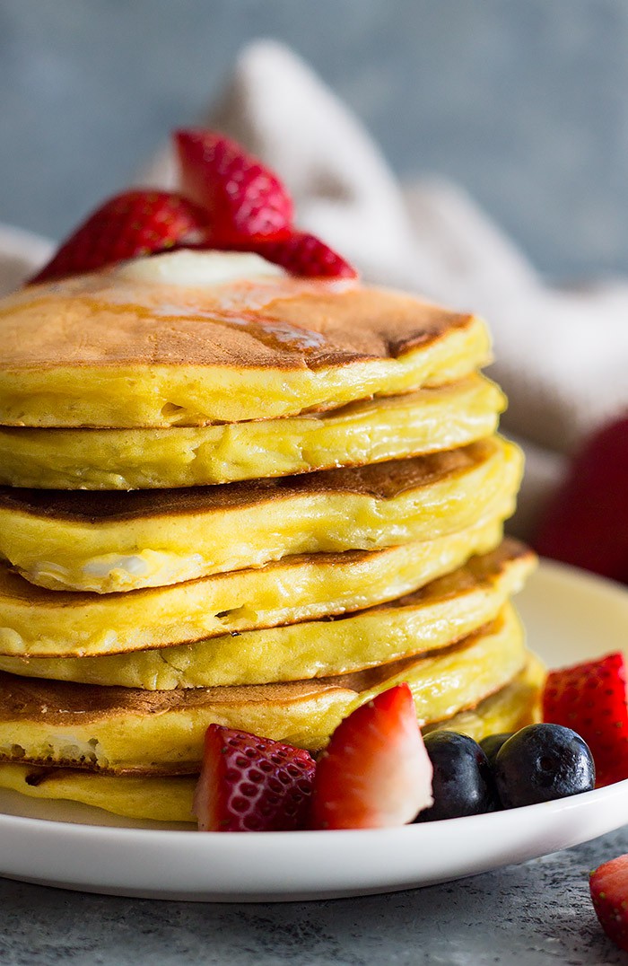 Tall stack of high protein cottage cheese pancakes with melted butter and chopped fruit. 