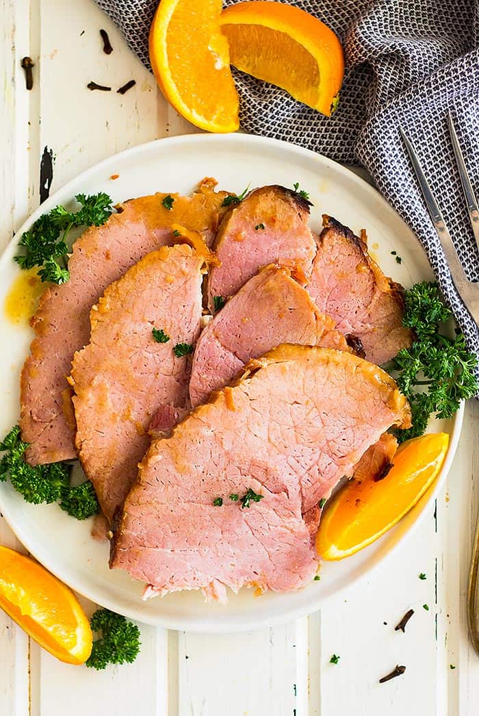 Slow cooker honey mustard glazed ham sliced and on a plate. Garnished with parsley.