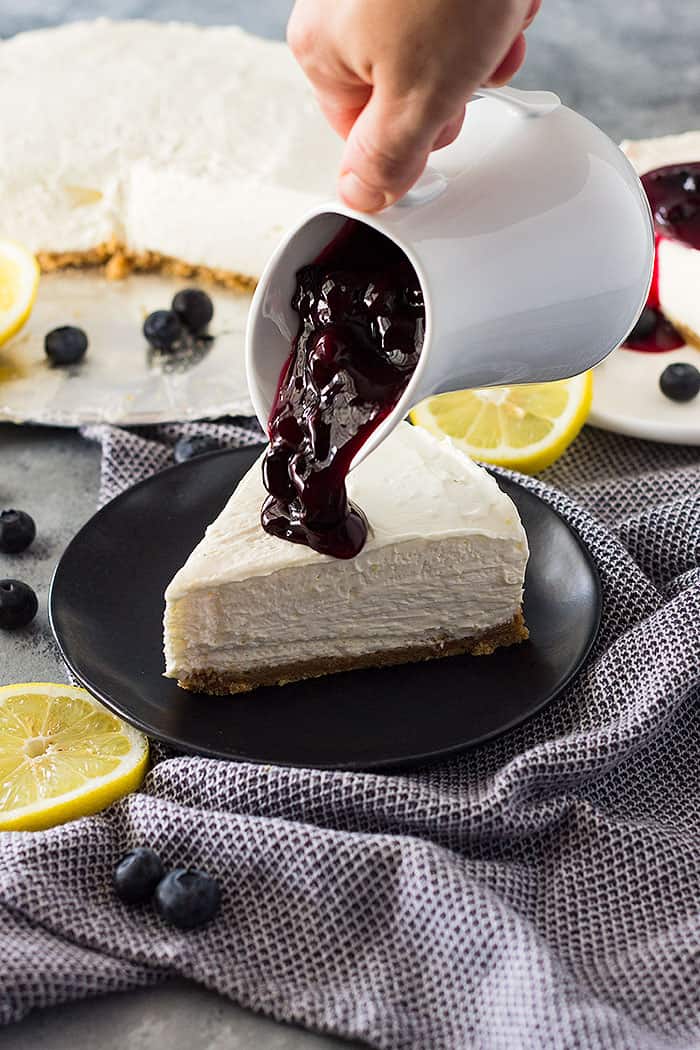 Slice of No Bake Lemon Blueberry Cheesecake with blueberry topping being poured on top.