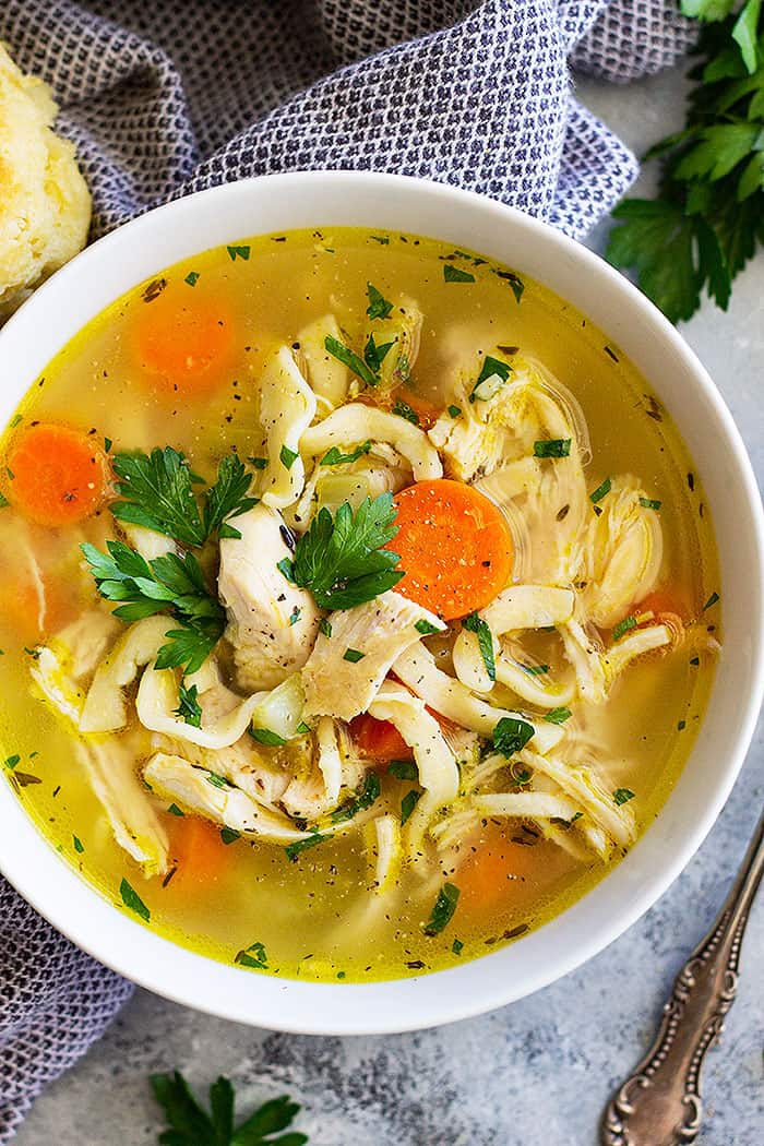 Close up of the whole chicken soup in a white bowl.