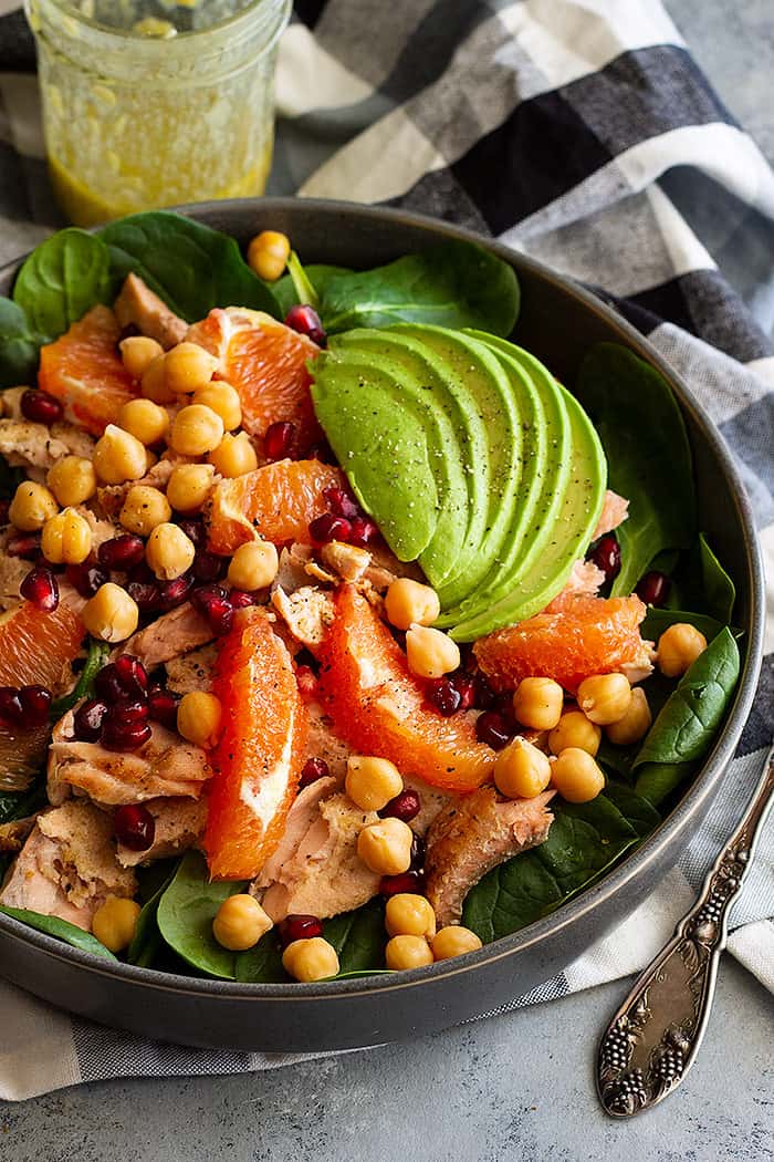 A large bowl of spinach salad with salmon and avocado sprinkled with pepper.