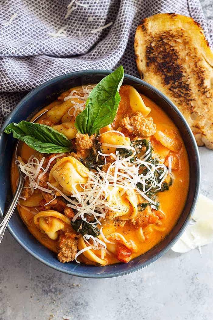 Top down view of tortellini soup in a blue bowl topped with cheese. 