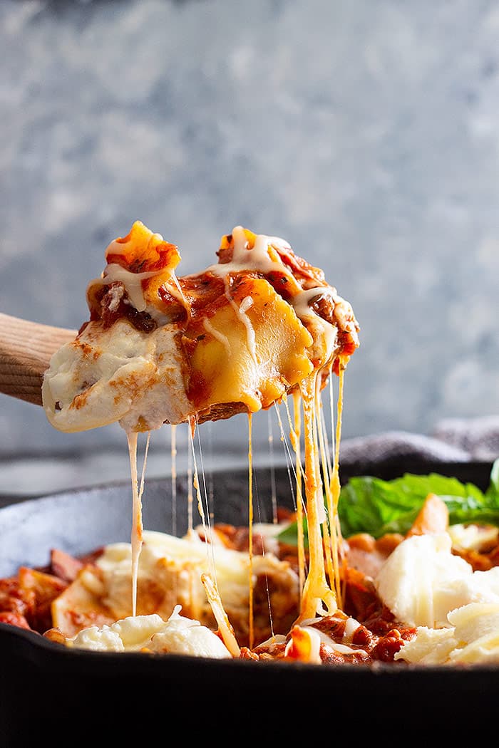 A large spoon serving skillet lasagna with a huge cheese pull. 