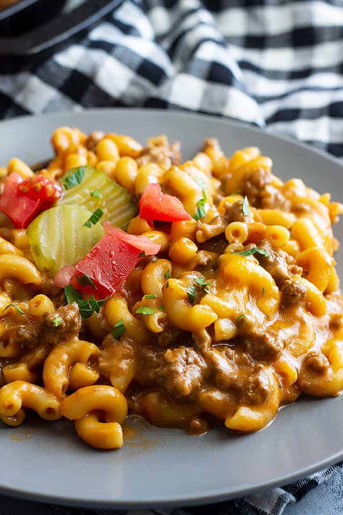 A close up of cheeseburger pasta on a plate topped with chopped tomato and pickles. 