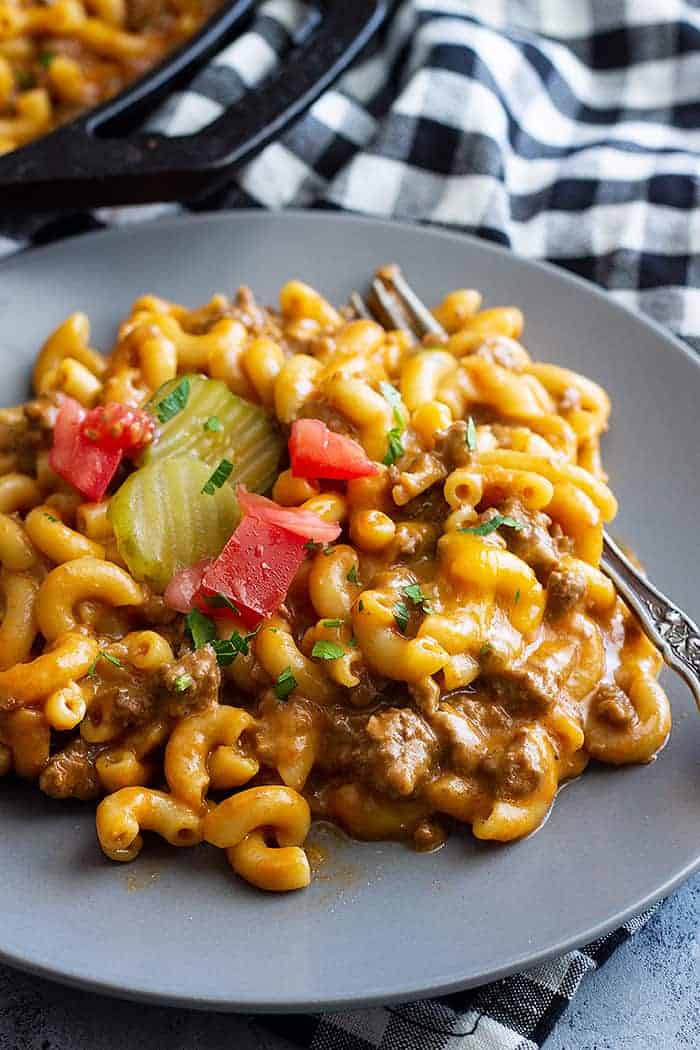 A plate of cheeseburger pasta topped with chopped parsley and tomato. 