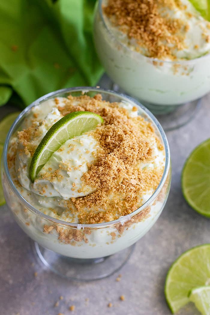 Lime cheesecake fluff in a dessert bowl topped with graham cracker crumbs and a lime wedge.