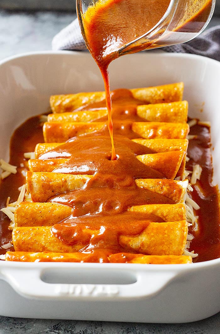 Homemade enchilada sauce being poured over cheese enchiladas. 