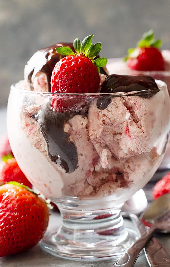 Strawberry ice cream in a dessert cup topped with hot fudge sauce and a fresh strawberry. 