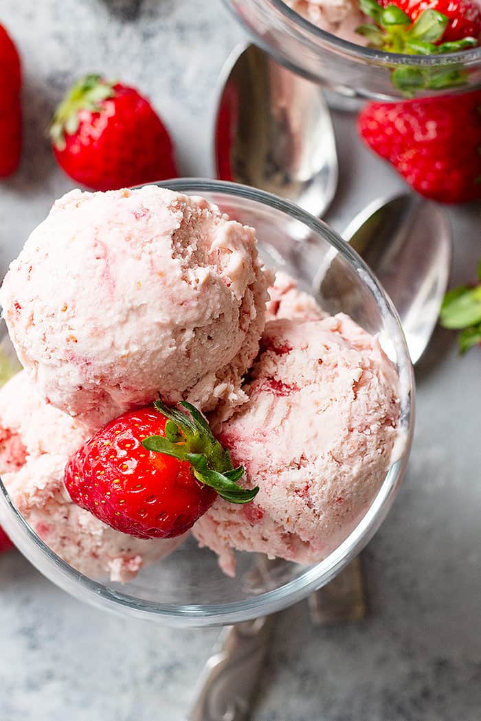 A top down view of scoops of strawberry ice cream in a bowl and topped with a strawberry. 