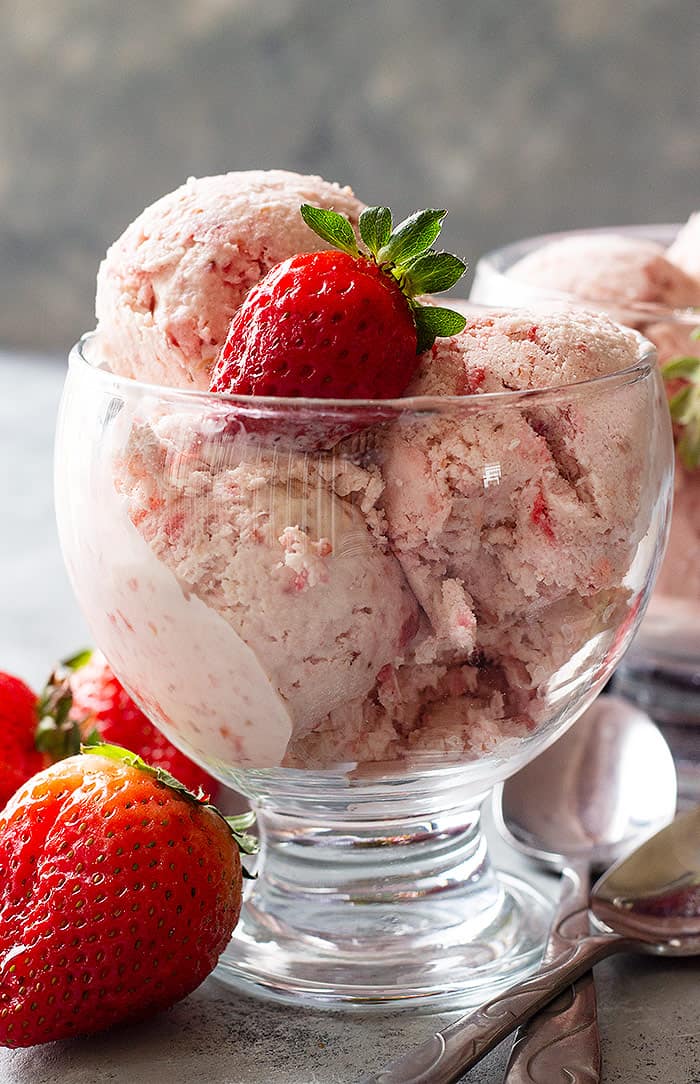 A dessert cup filled with scoops of strawberry ice cream and topped with a fresh strawberry. 